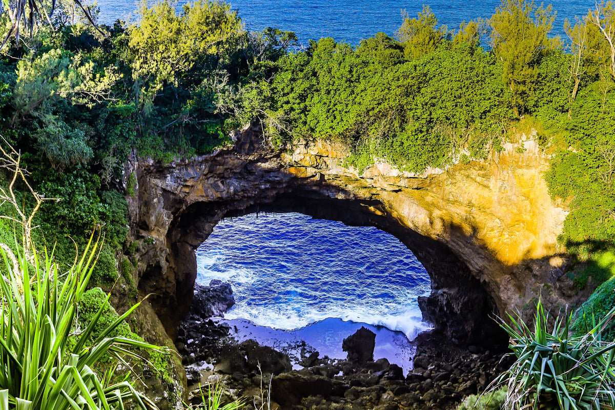 Natural rock formation with a cave overhanging a body of water surrounded by greenery.