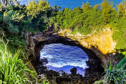 Natural rock formation with a cave overhanging a body of water surrounded by greenery.