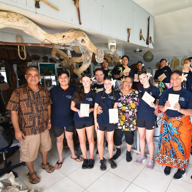 A group of people standing together inside a shop or workshop, holding small white certificates. Several individuals are wearing matching dark navy blue polo shirts with white logos, while others wear casual clothing.